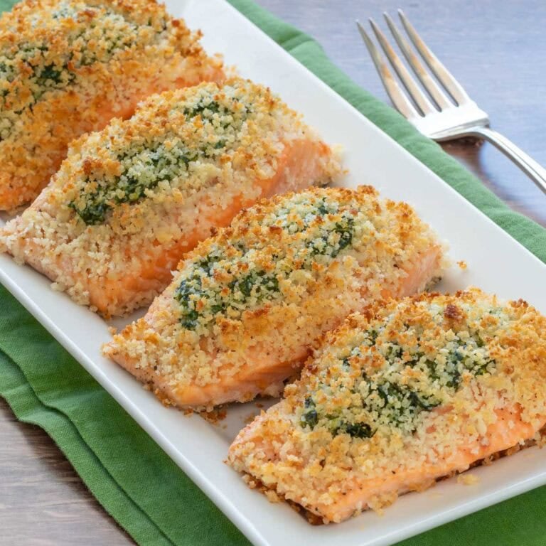 White serving platter holding 4 servings of Spinach Stuffed Salmon, with a serving fork alongside and plates in the background