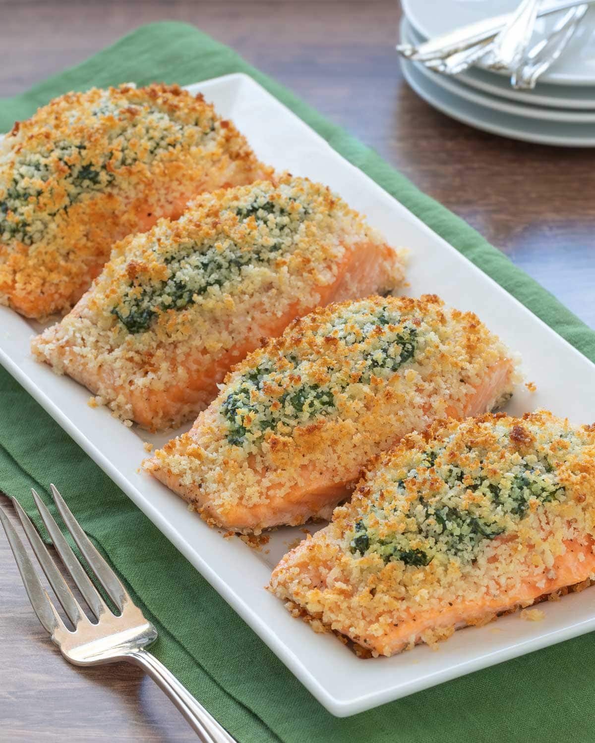 White serving platter holding 4 servings of Spinach Stuffed Salmon, with a serving fork alongside and plates in the background