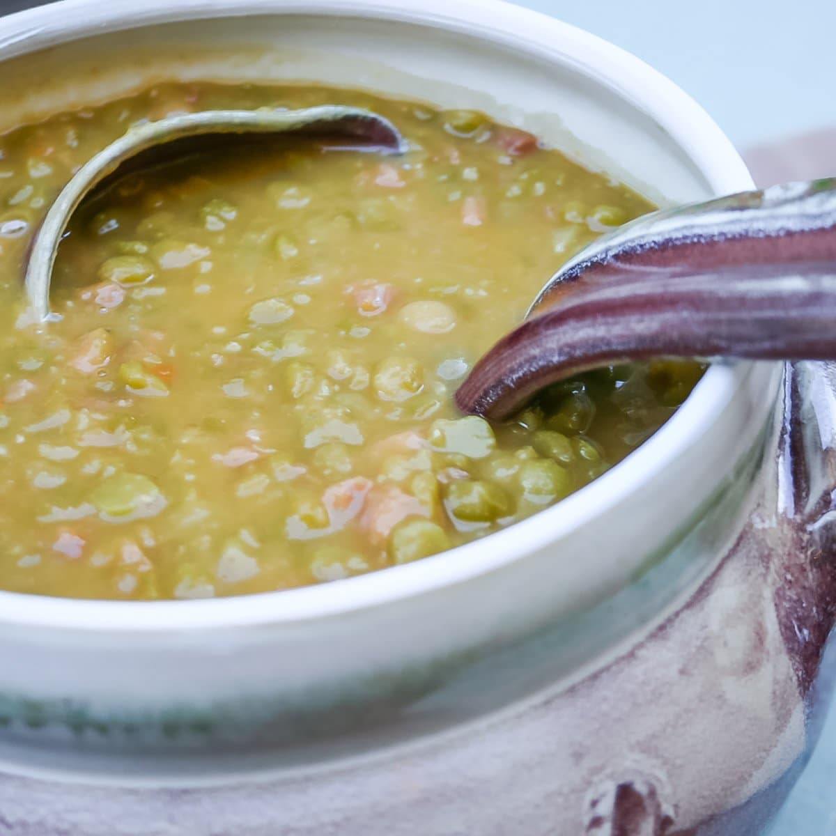 Soup tureen holding split pea soup with ham, with a ladle in the soup. Shows the soup's texture.