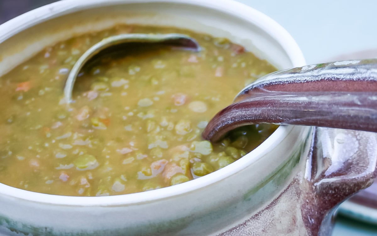 Soup tureen holding split pea soup with ham, with a ladle in the soup. Shows the soup's texture