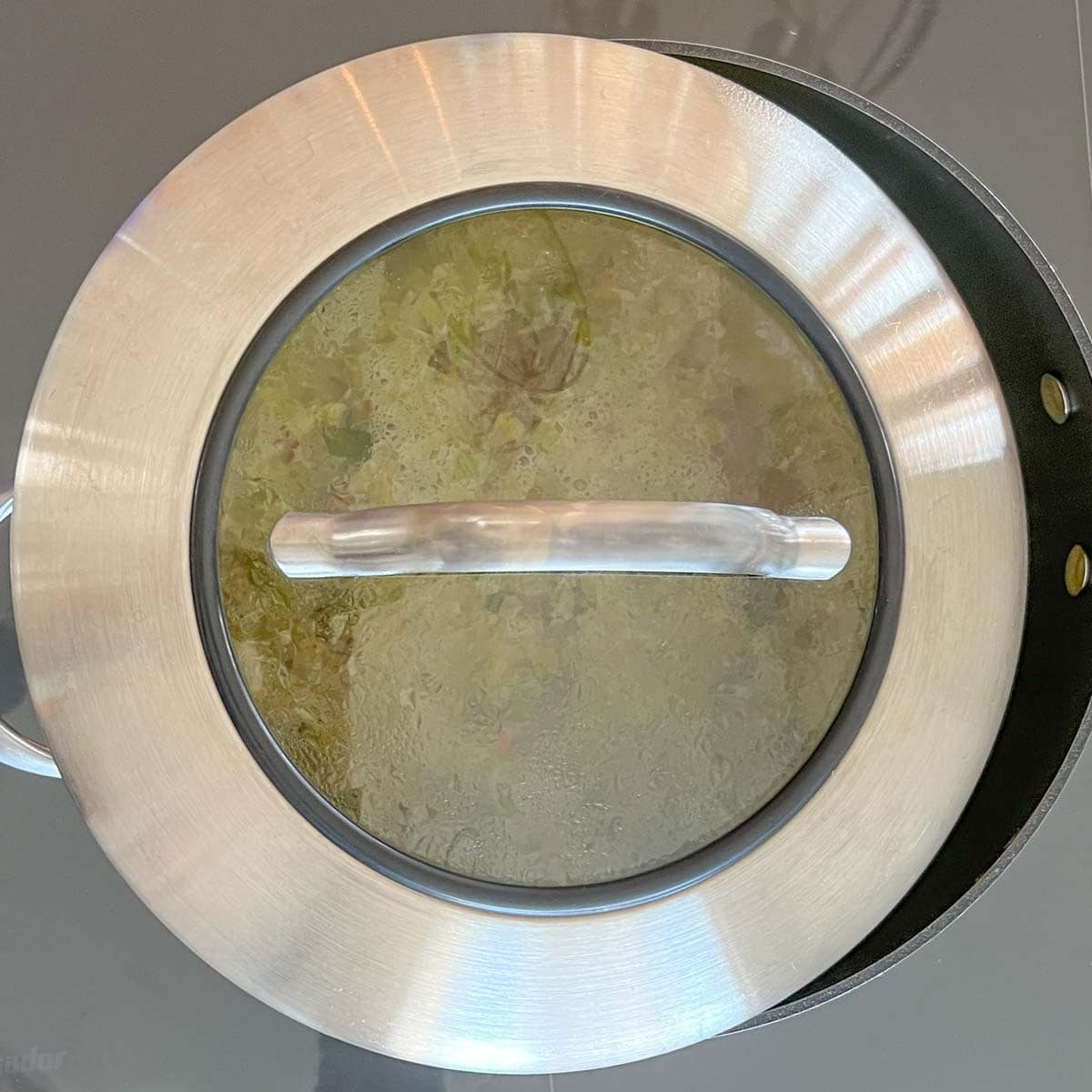 overhead view of broth and vegetables simmering. Shows how the lid partially covers the skillet.