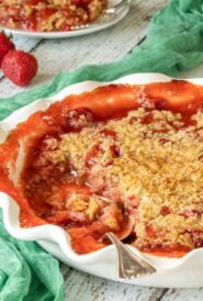 Strawberry Rhubarb Crisp in a white pie plate with a scoop removed, and a spoon in the plate