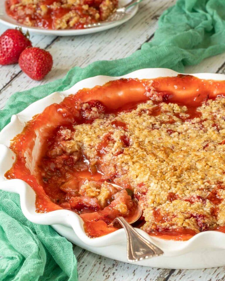 Strawberry Rhubarb Crisp in a white pie plate with a scoop removed, and a spoon in the plate