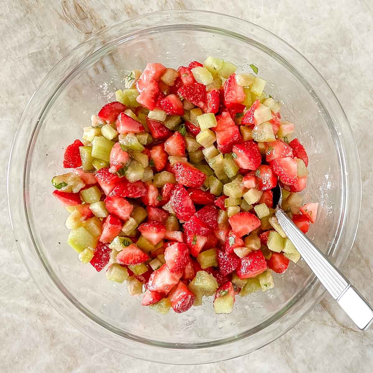 glass bowl holding Strawberry Rhubarb Crisp filling ingredients that have been mixed with a spoon