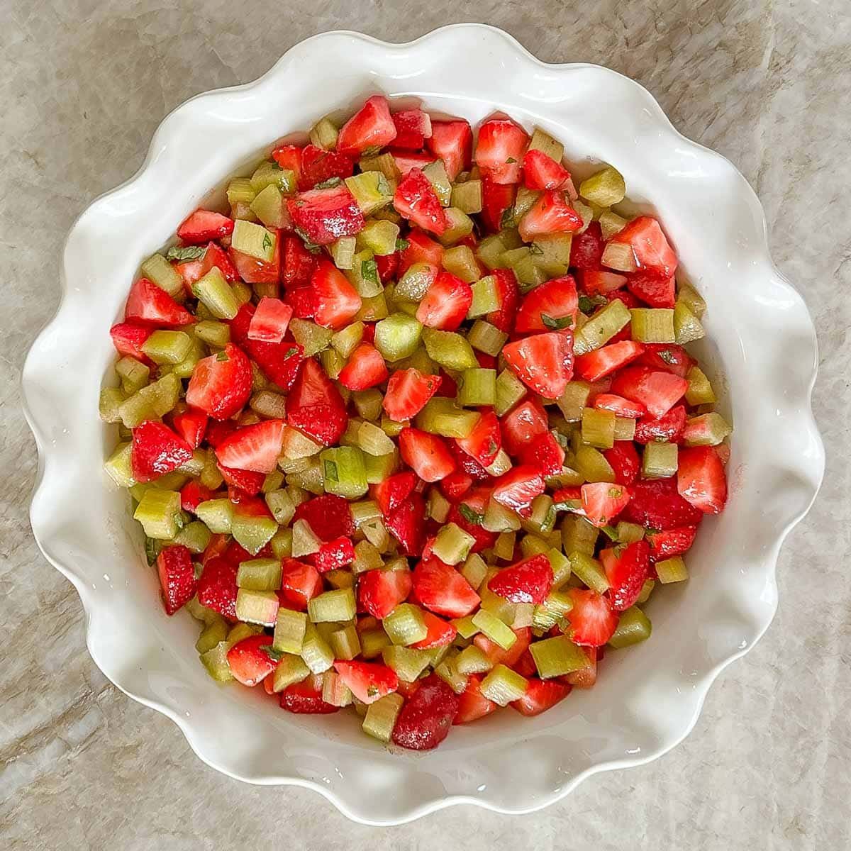 White deep dish. pie plate holding the Strawberry Rhubarb Crisp filling