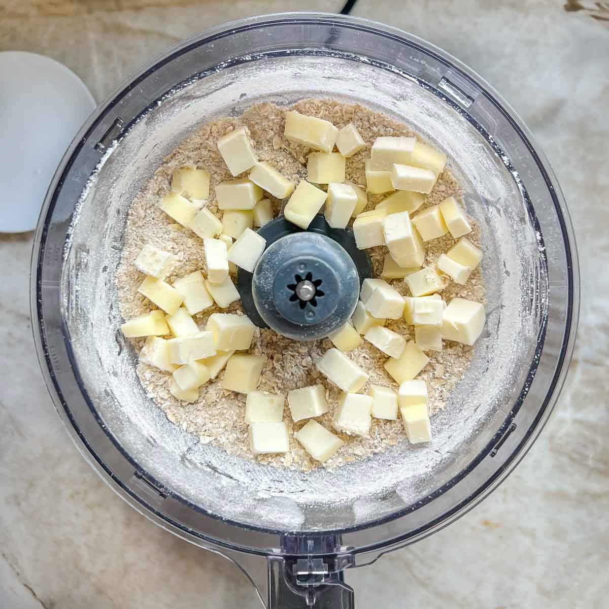Food processor with cubed cold butter atop the other mixed topping ingredients