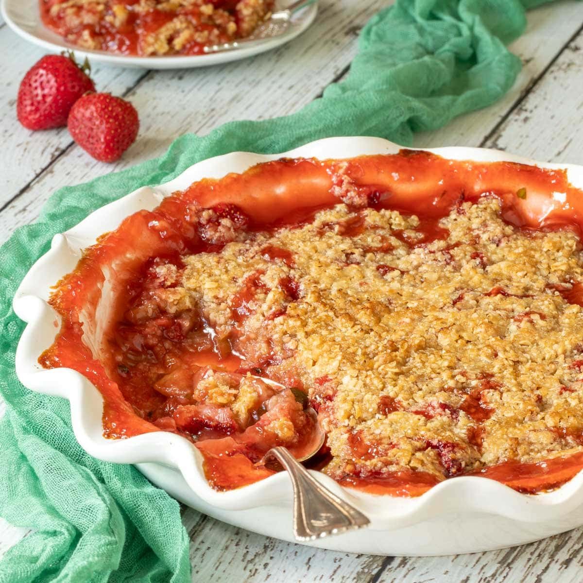 Strawberry Rhubarb Crisp in a white pie plate with a scoop removed, and a spoon in the plate