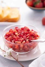 Close up of glass bowl showing Strawberry Topping, with sliced cake in the background