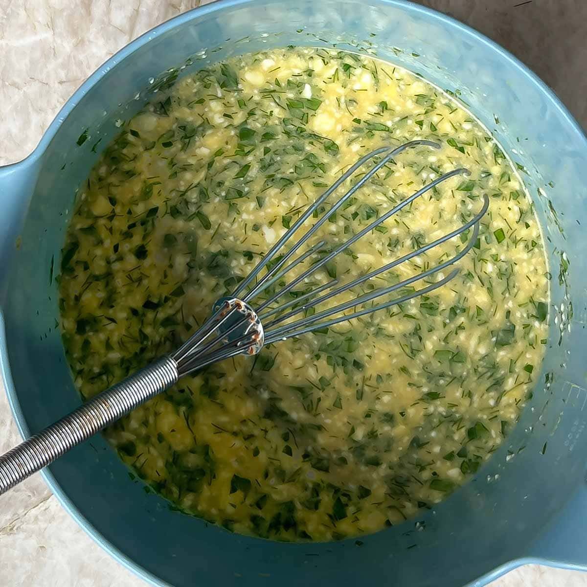 Blue bowl holding tomato feta frittata egg mixture with a whisk in the bowl
