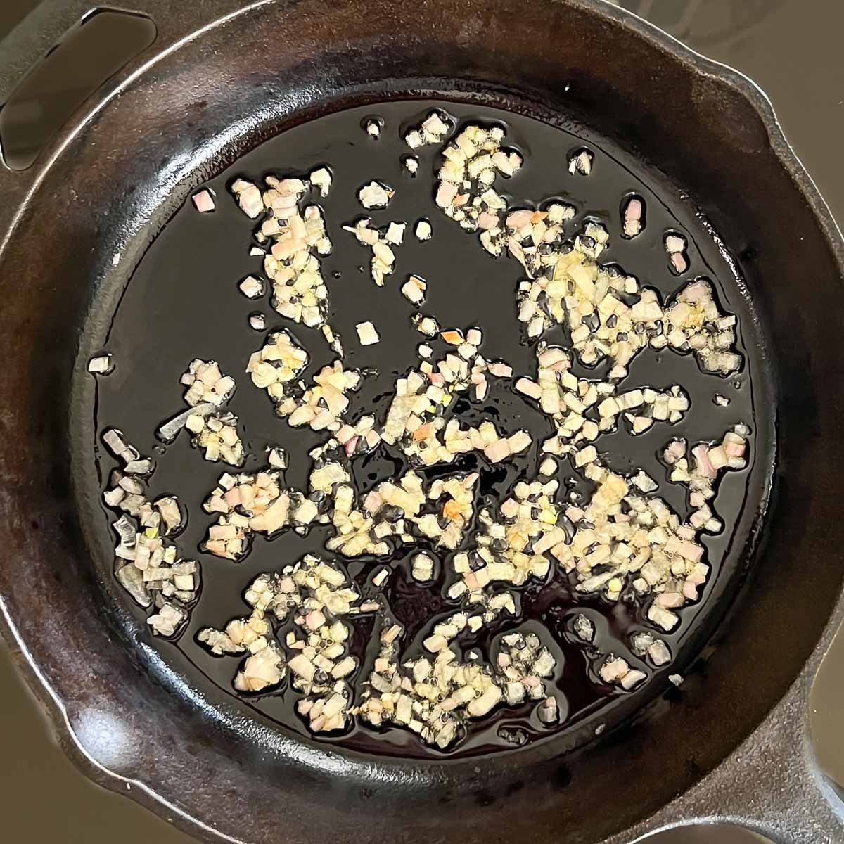Chopped shallots cooking in olive oil in a cast iron skillet