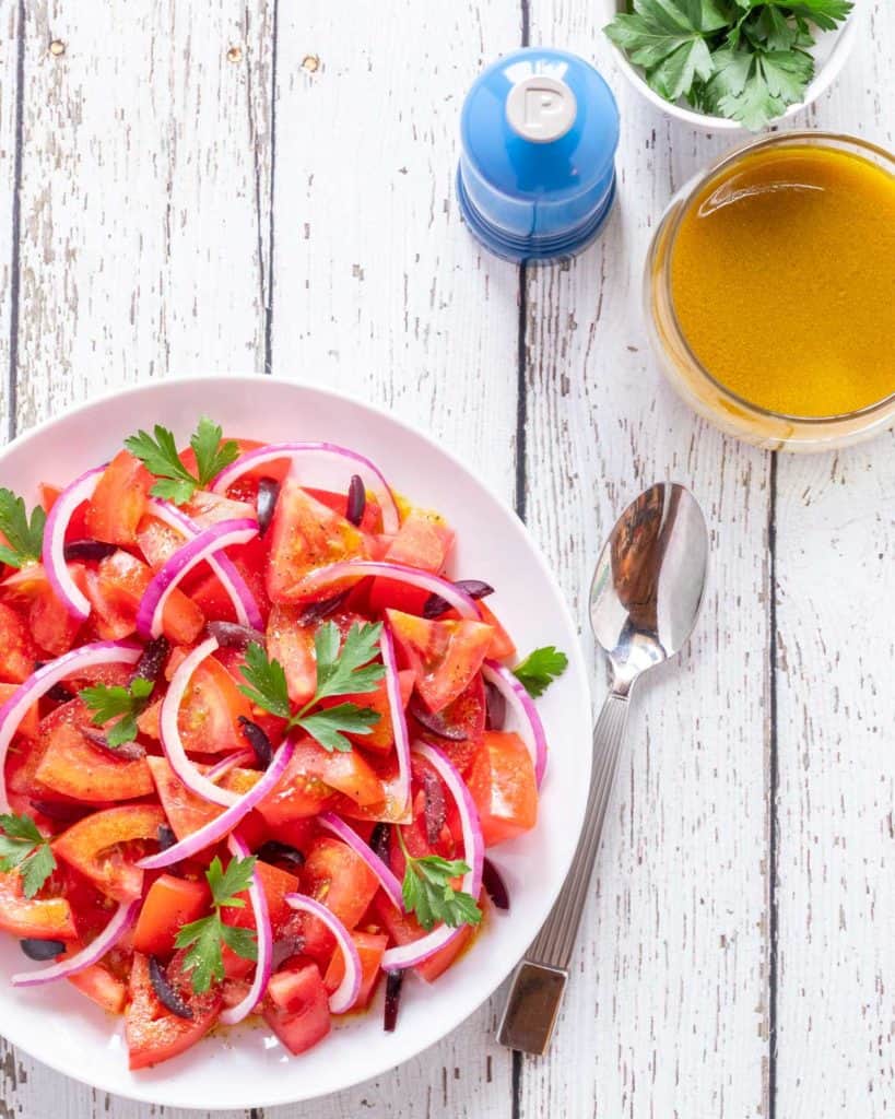 white plate showing Tomato Salad Recipe, with a spoon, Cumin Dressing and a pepper mill on the side