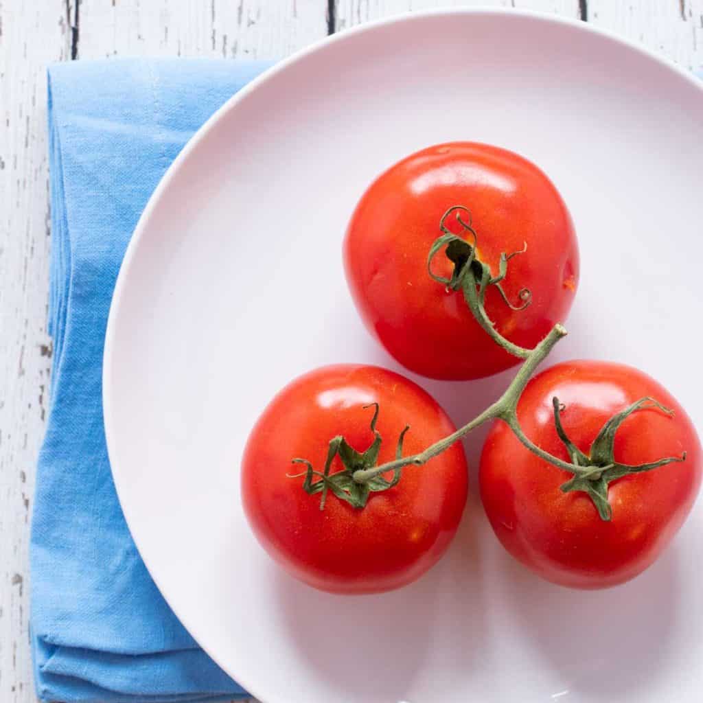 white plate holding three tomatoes on the vine