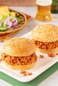 two turkey sloppy joes on a white platter with toppings and a beer in the background