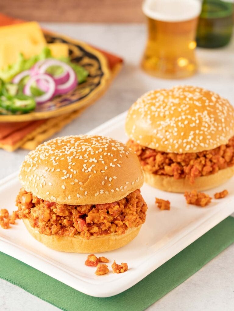 two turkey sloppy joes on a white platter with toppings and a beer in the background