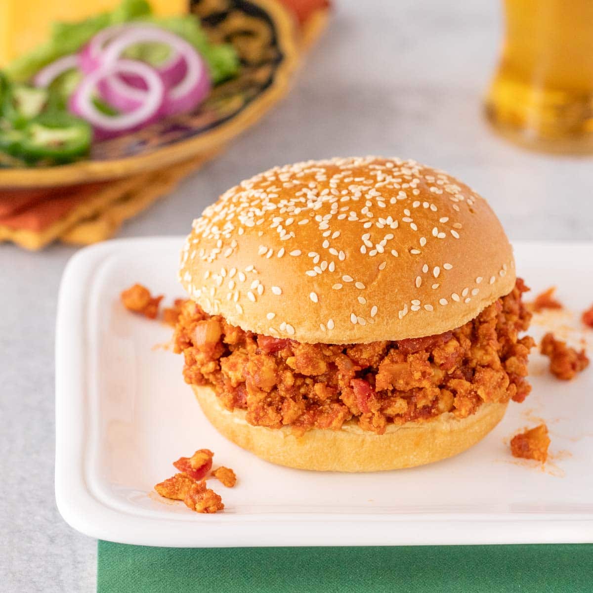 one turkey sloppy joe on a white platter with toppings and a beer in the background