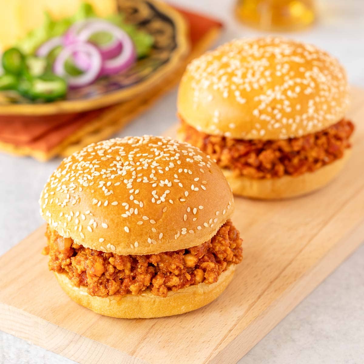 two turkey sloppy joes on a white platter with toppings and a beer in the background