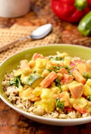 bowl holding a portion of Mixed Vegetable Curry on brown rice, with a spoon in back