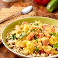 bowl holding a portion of Mixed Vegetable Curry on brown rice, with a spoon in back