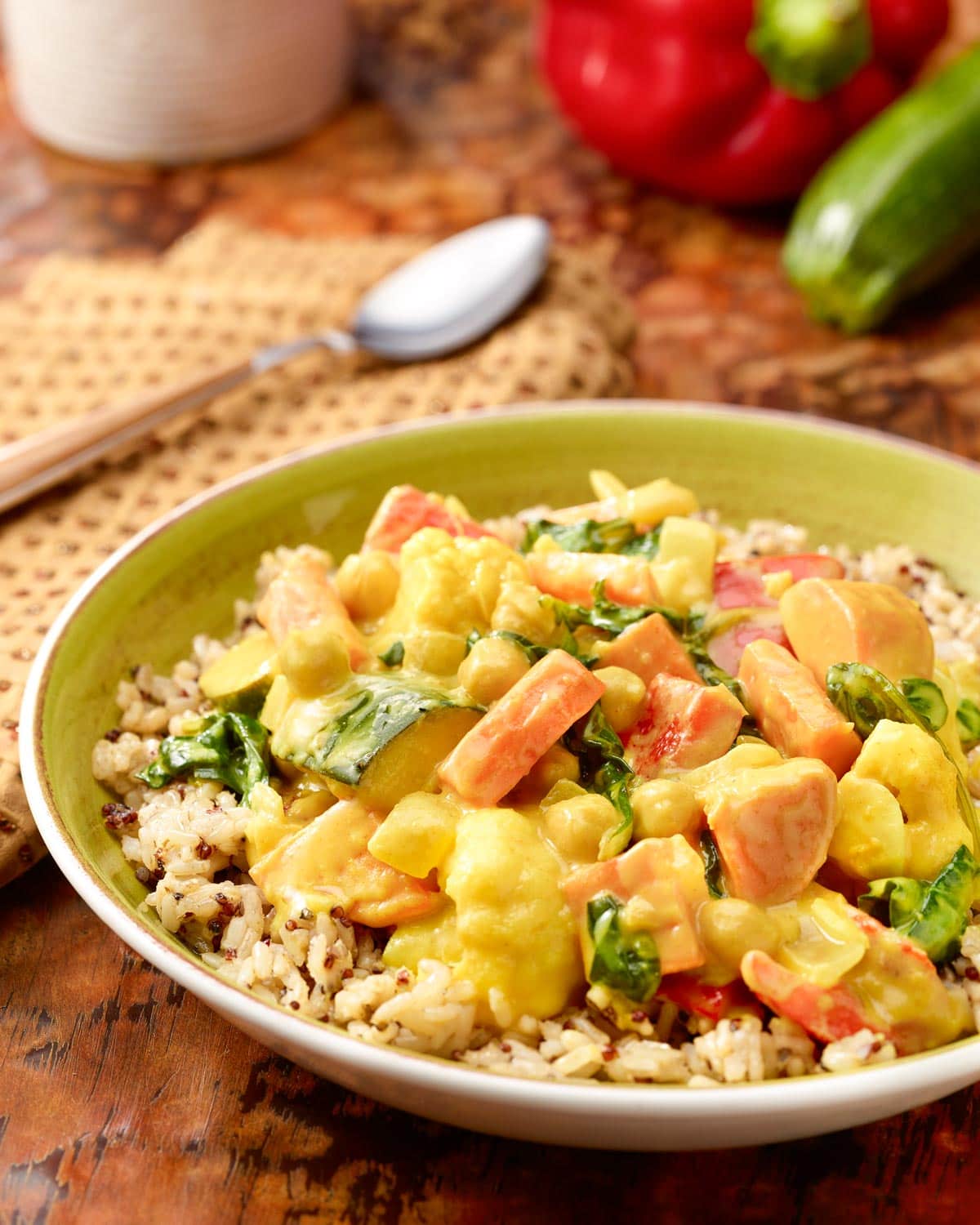 bowl holding a portion of Mixed Vegetable Curry on brown rice, with a spoon in back